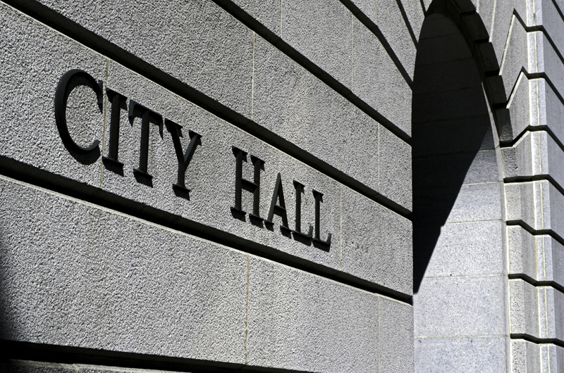 The stone side of an entrance to a city hall building, with a "City Hall" sign.